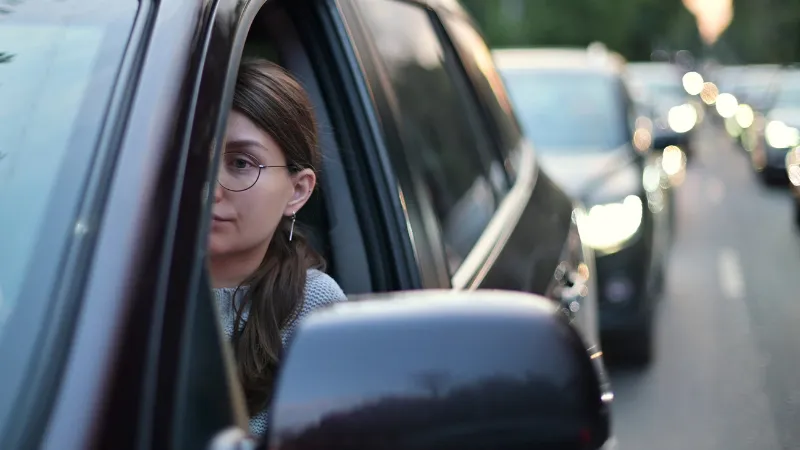 A young woman sits in a car during rush hour. Woman wasting time in traffic