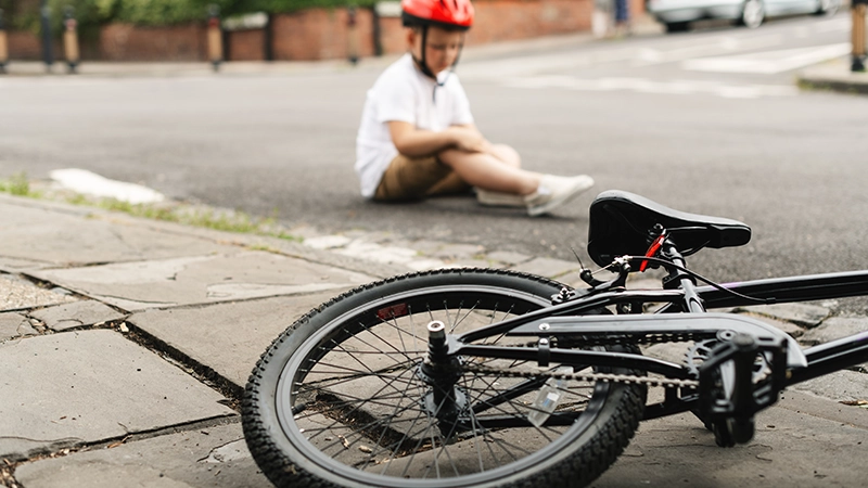 A child wearing a red helmet sits on the street after a bike accident.