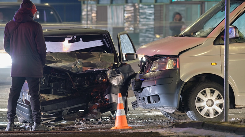 Cars crashed heavily in road accident after collision and silhouette of people on city street at night.