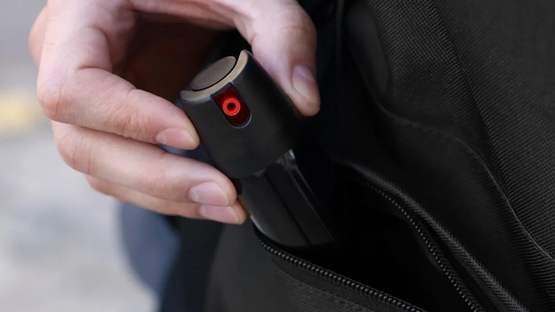 a person's hand holding a small, black, cylindrical object with a red dot on it, and it is being placed into or taken out of a black bag.