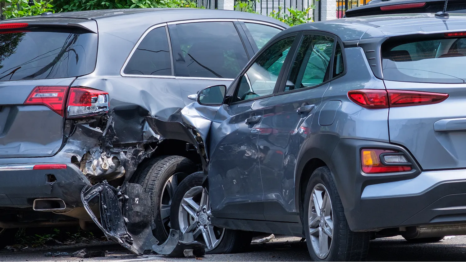 A rear-end collision, one gray SUV is heavily damaged in the front, and another gray SUV has significant damage to its rear.