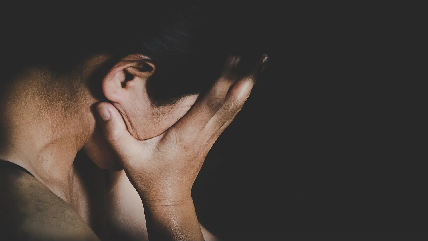 A person from the shoulders up, with their face obscured by one of their hands.
