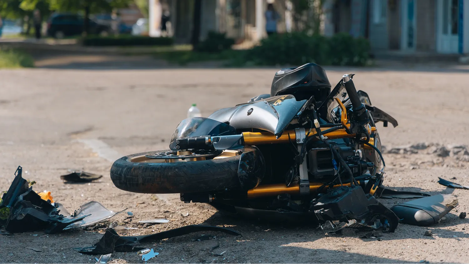 a severely damaged black and gold motorcycle lying on its side on a dirt and asphalt surface.