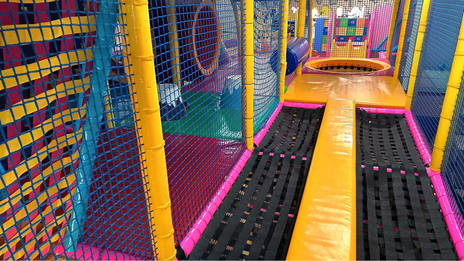 A vibrant, colorful indoor play area, specifically a trampoline and obstacle course section.