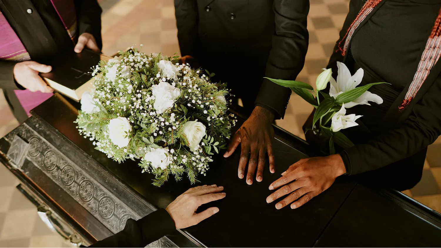 The individuals are dressed in dark, formal attire, with one person wearing a black suit and another in a black outfit with a beaded or textured top.