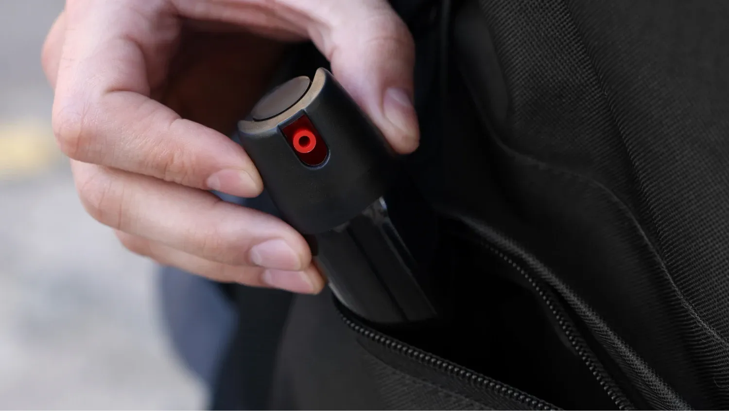 a person's hand holding a small, black, cylindrical object with a red dot on it, and it is being placed into or taken out of a black bag.
