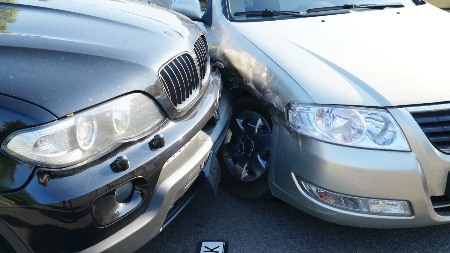Two cars, one dark-colored and one light-colored, are shown with their front ends touching, indicating a collision.