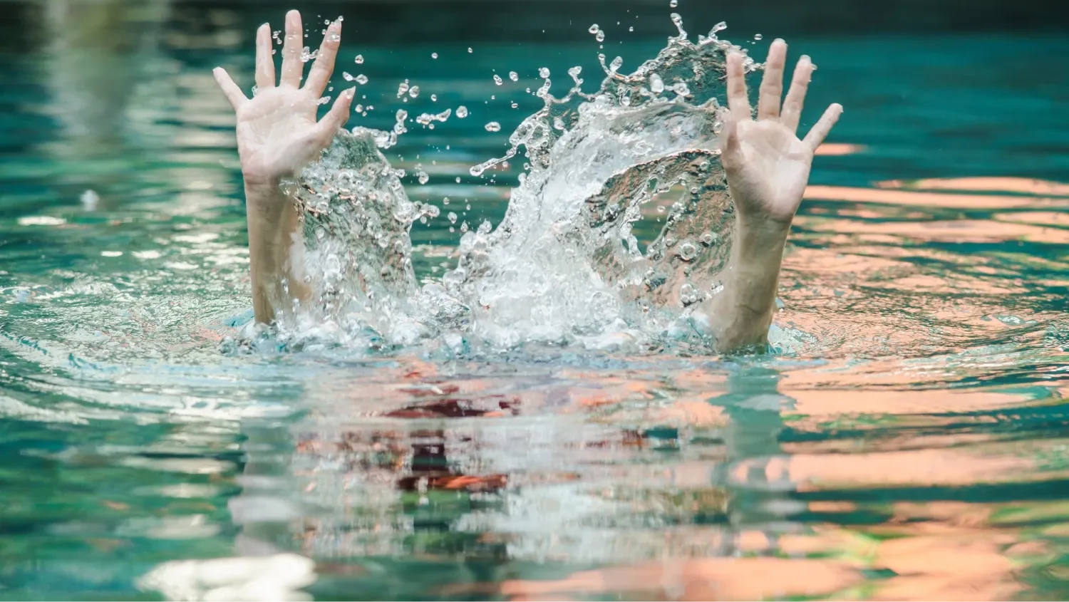 A person's arms and hands raised out of the water, palms open, in a gesture that suggests they are struggling or drowning.